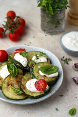 Zucchini fried on a plate with basil and cherry tomatoes, sour cream sauce and spices in bowls, cherry sprigs, herbs, pepper mill.