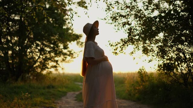 A pregnant woman clutches her stomach at sunset