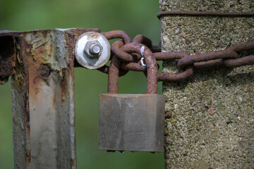 Weathered metal garden gate, closed with a rusty chain and an old padlock against a green background, copy space, selected focus