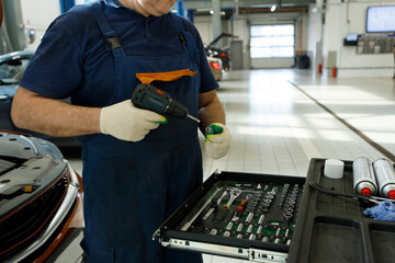 professional mechanic with a pneumatic screwdriver selects an attachment in a cabinet with tools in...