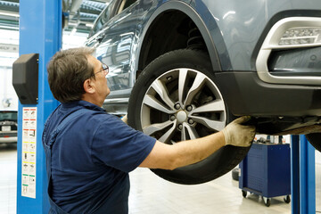 car mechanic at repair service station inspecting car wheel and suspension detail of lifted...