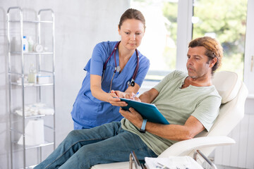 Obraz premium Adult female doctor in medical uniform signing contract with adult male patient in medical room