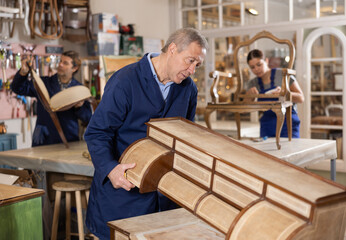 Mature male carpenter working on making vintage commode in workshop