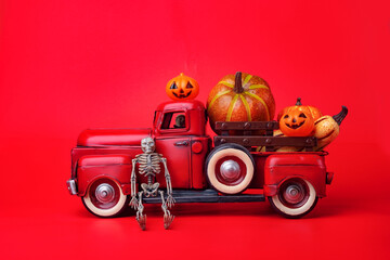 Happy Halloween, orange pumpkins in red toy truck with human skeleton on red background.