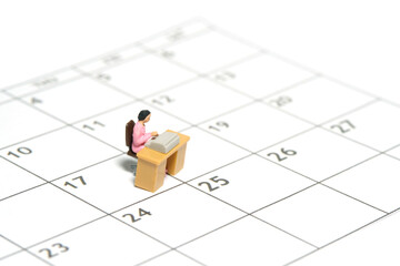 Miniature tiny people toy figure photography. Work schedule management concept. A businesswomen seat on his desk, above calendar. Isolated on a white background.