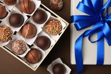 Box with delicious chocolate candies on brown background, flat lay