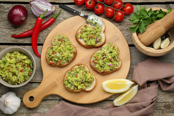 Slices of bread with tasty guacamole and ingredients on wooden table, flat lay