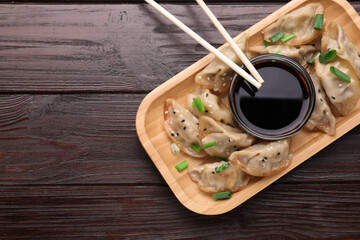 Delicious gyoza (asian dumplings) with green onions, soy sauce and chopsticks on wooden table, top view. Space for text