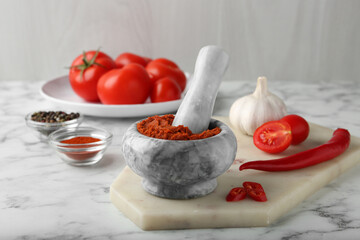 Red curry paste in mortar and ingredients on white marble table