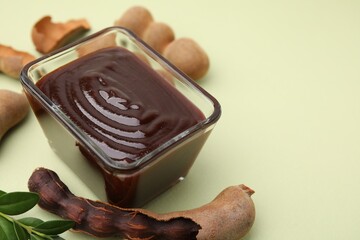Bowl of tasty tamarind sauce, leaves and fresh pods on light green table. Space for text