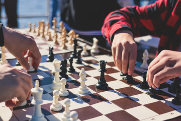 Chess tournament, kids and adults participate in chess match game outdoors in a summer sunny day, players of all ages play, competition in chess school club with chessboards on a table