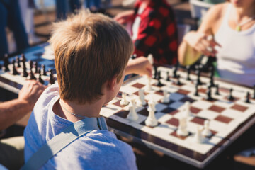 Chess tournament, kids and adults participate in chess match game outdoors in a summer sunny day, players of all ages play, competition in chess school club with chessboards on a table