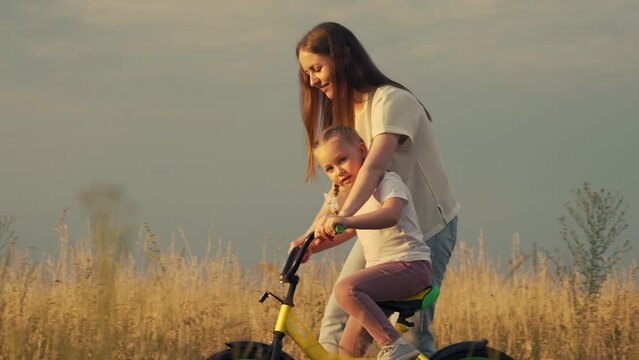 Caring mother teaches daughter to ride bicycle along rural road across field