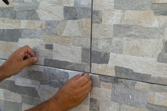Image of the hands of a tiler mason inserting shims into freshly laid tiles. Do-it-yourself work, renovation and installation of a house floor.