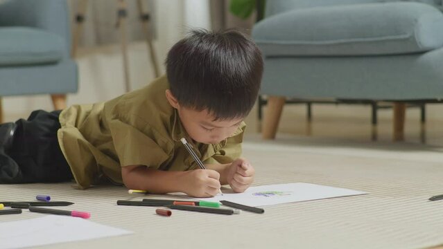 Close Up Of Asian Kid Lying On The Floor Drawing At Home
