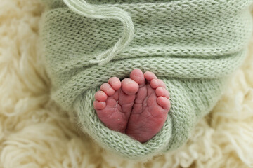 Tiny foot of a newborn. Soft feet of a newborn in a green, pistachio, olive woolen blanket on a white flaccati background. Macro photo of the toes, heels and feet of a newborn. 