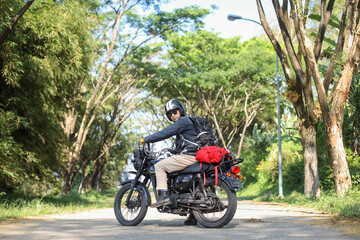 Biker wearing black leather jacket looking at camera while sitting on vintage motorcycle ready for adventure riding