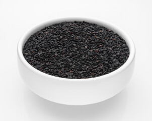 Black sesame seeds in a white bowl on a white background. Isolate. Selective focus. Close-up.