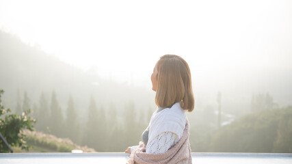 asian woman stands with her back to camera and enjoys the view of forest. and looking mountain view in morning sunrise with copy space. trip and relaxing. Travel vacations and lifestyle concept.