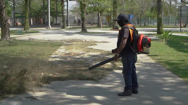 A gardener using a leaf blower to clear up leaves in a garden.