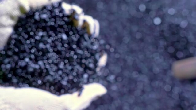 Slow motion 4k pours plastic granules in product line.Top view on gloves with black plastic recycling.Polymer composite raw material pours in container for mixing.Concept ecological plastic recycling