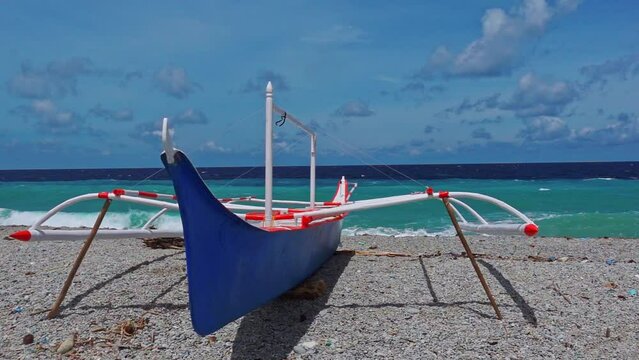A bright blue banka boast sitting on the beach against turquoise tropical waters. Philippines