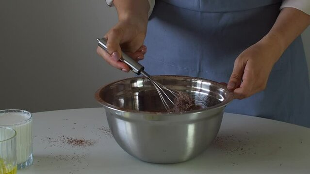A woman kneads dough for a cupcake, cake or brownie in a metal bowl with a whisk. Preparation of dough for birthday cakes. A step for making muffins, pie, sponge cake. Baking process step by step.