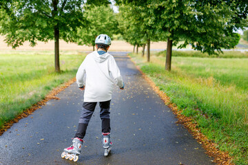 Active school boy skating in summer park, healthy lifestyle for children. Happy teenager with inline skaters, having fun with making sports.