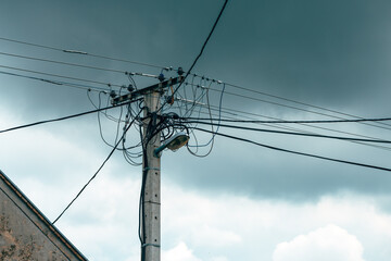 Old power utility and street light pole with cables and wires against dramatic sky