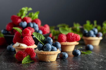 Small tartlets with fresh raspberries and blueberries on a black background.