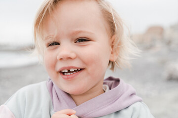 Close-up portrait of a little girl on a pebble beach in a hoodie