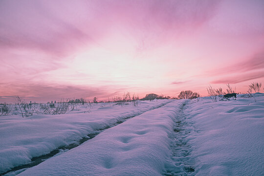 Winter field landscape with path at sunset.