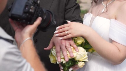 the bride and groom in wedding suits pose for a photographer at a photo shoot showing wedding rings. the photographer shoots a wedding celebration.