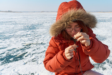 Woman in warm clothes on frozen lake,  winter fishing