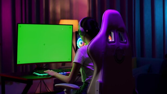Asian Teen Girl Gamer Wearing Head Phones And Play Video Game On Computer With Mock Up Green Screen
