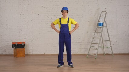 Full length shot of a smiling young construction worker standing in the room under renovation with his hands on his hips.