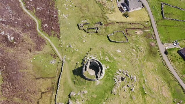 Drone shot from a birds-eye-view perspective of the Carloway Broch with surrounding stone black houses. Filmed on the west side of the Isle of Lewis, part of the Outer Hebrides of Scotland.