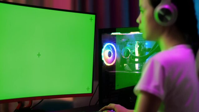 Close Up Of Excited Asian Teen Girl Gamer Celebrates Victory And Dancing While Playing Video Game On Computer With Mock Up Green Screen
