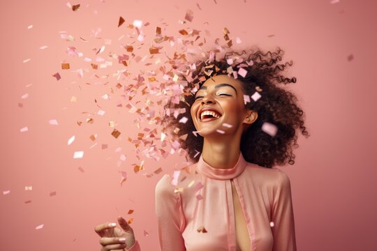 Fun party girl, smiling woman throwing confetti on a pastel pink background. Composition for birthday or woman's day. Party time concept.