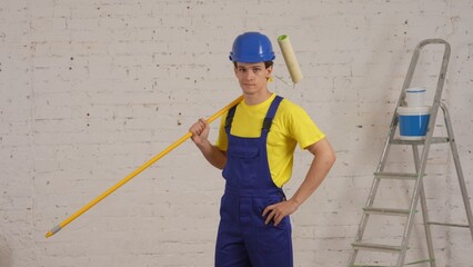 Medium shot of a smiling young worker standing in the room with a roller placed on his shoulder and looking straight at the camera.