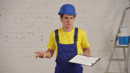 Medium shot of a young construction worker standing in the room, holding a planchette, folder and a...