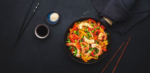 Stir fry shrimps with  red paprika, green peas, chives and sesame seeds in frying pan. Asian cuisine dish. Black kitchen table background, top view - obrazy, fototapety, plakaty