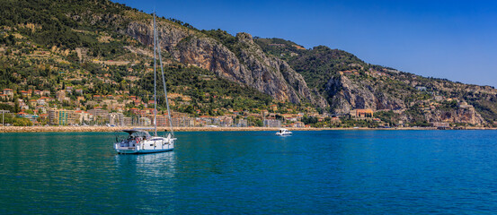Fototapeta premium Mediterranean Sea and coastline with a beach and a boat in the water in Menton on the French Riviera, South of France on a sunny day