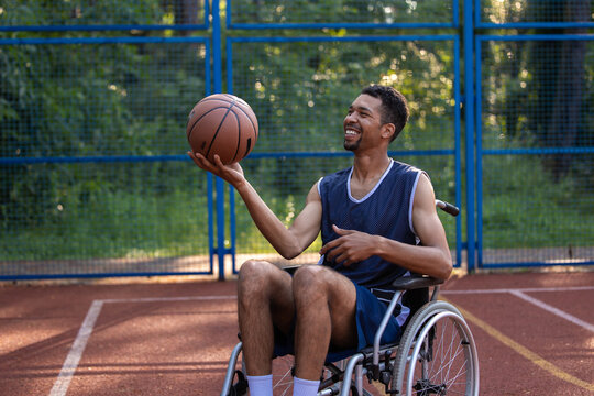 Happy basketball player with disability uses wheelchair while playing on sports court.