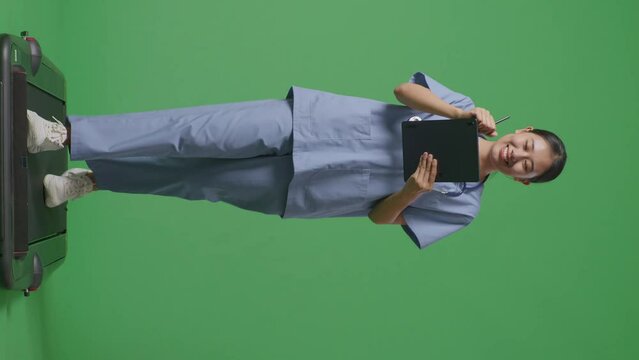 Full Body Of Asian Female Doctor With Stethoscope Taking Note On A Tablet While Walking On Green Screen Background In The Hospital
