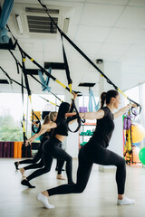 Group of active sports girls in black sportswear are engaged in budgie fitness in the gym. Bungee jumping in the gym