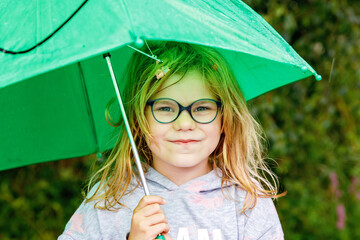 Little preschool girl walking during rain with big green umbrella on rainy day. Happy positive...