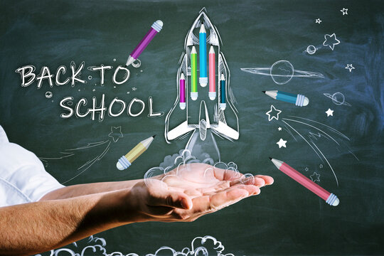 Close up of hands holding abstract back to school sketch with pencils and rocket on chalkboard wall background. Education and knowledge concept.