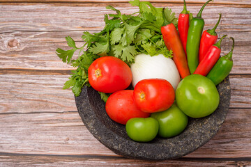 Molcajete with vegetables on wooden table. Ingredients for a hot sauce.