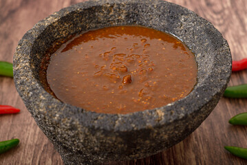 Molcajete with hot sauce on wooden table with chili peppers around.